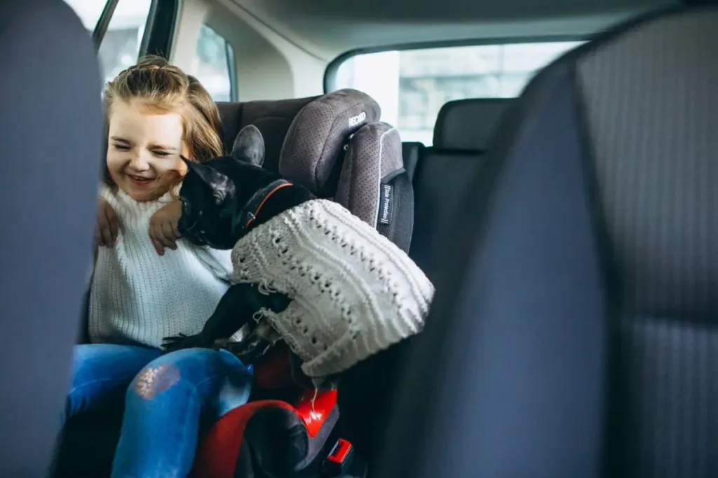 A young girl enjoying a car ride with her pet dog while seated safely in a 3 in 1 car seat.
