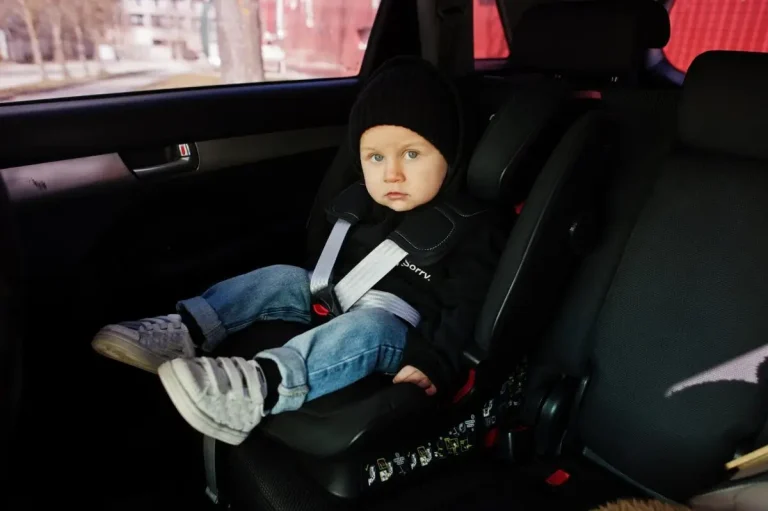 A young child wearing a black beanie and jeans seated securely in a baby car seat inside a car.