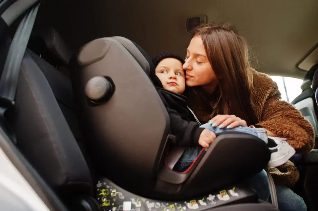 A mother with her baby, safely strapped in a car seat ensuring child safety during car travel. 