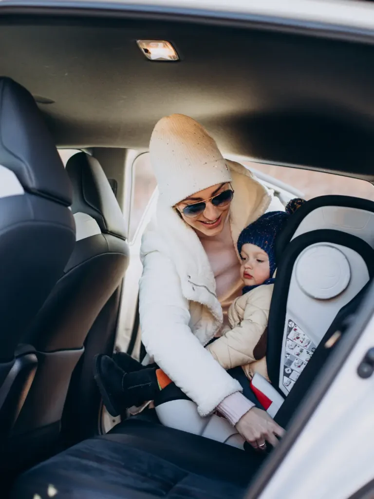 Mother securing her child in a car seat. It demonstrates the importance of considering safety features available in a baby car seat while choosing a car seat for your child.