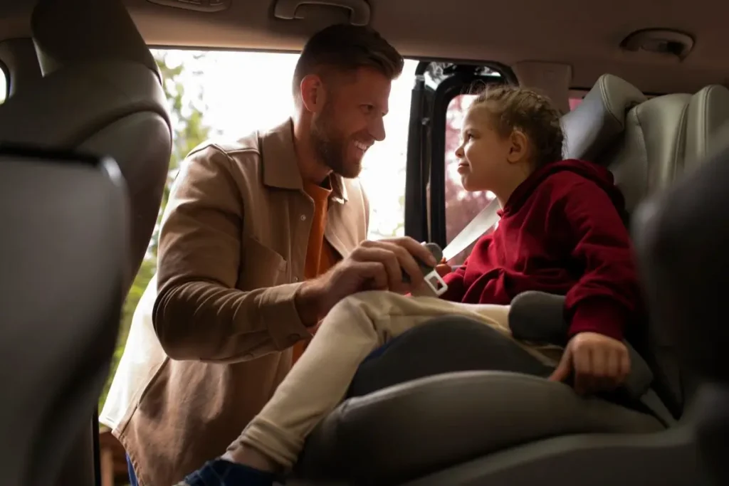 A smiling father securing his child in a combination car seat inside a vehicle for a safe journey.
