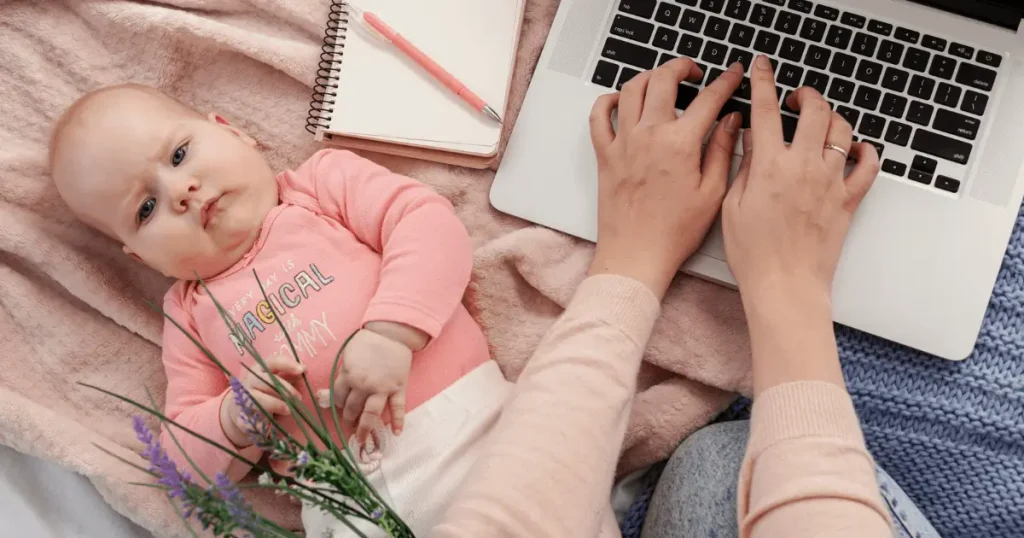 Mother typing with baby beside her, symbolizing support at The Baby Gear Land.