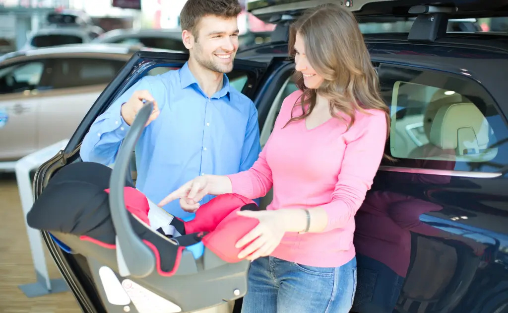 A smiling couple learning how to install an infant car seat in their car.