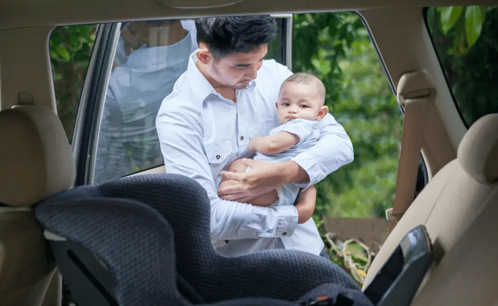 A father ready to secure his child in a convertible car seat installed in a rear-facing position.