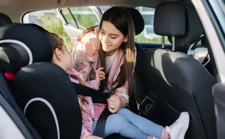 A mother happily securing her child in a booster car seat.