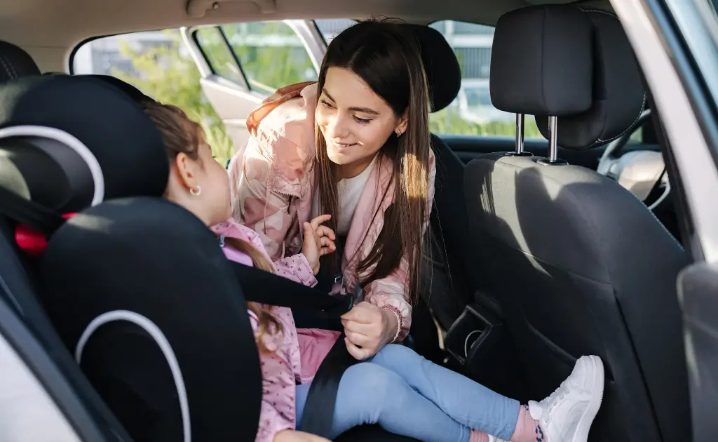 A mother happily securing her child in a booster car seat.