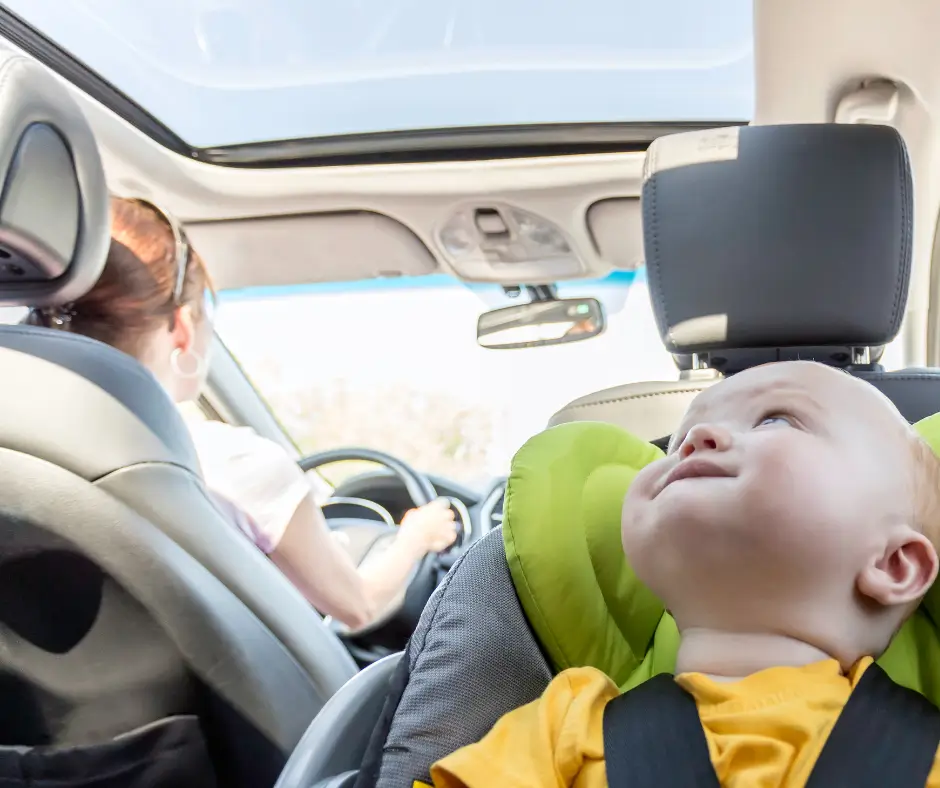 Rear-facing toddler in a convertible car seat during car ride with mother driving.