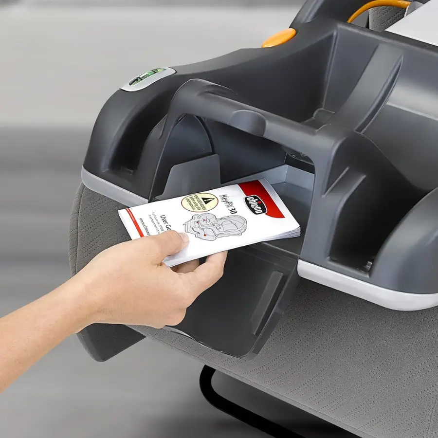 Hand placing user manual into storage compartment on Chicco KeyFit 30 car seat base.