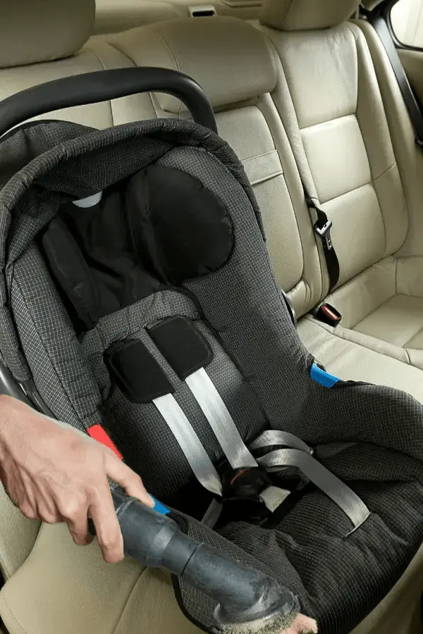 Vacuuming crumbs and dirt from a baby car seat placed in a car&rsquo;s backseat.